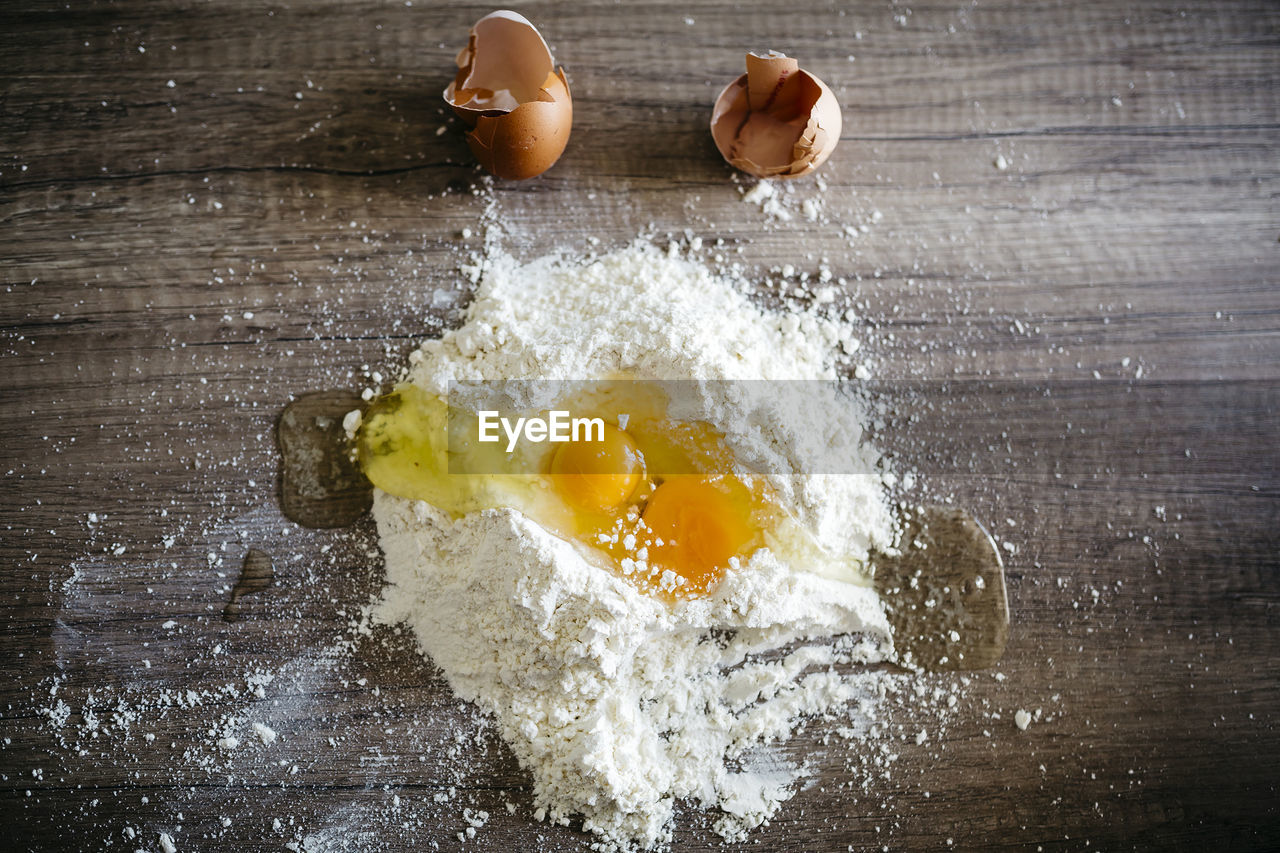 High angle view of eggs in flour on wooden table