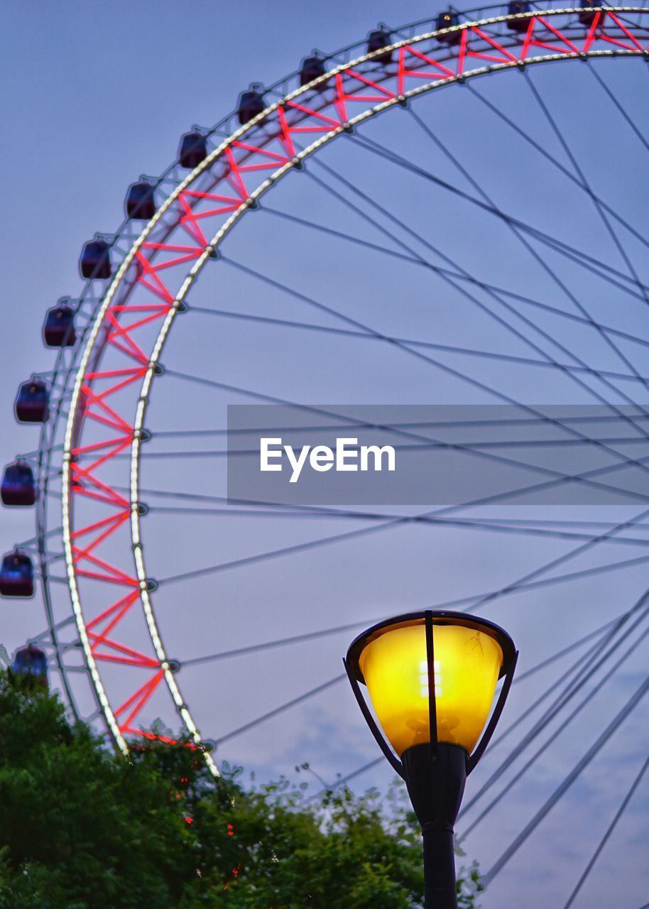 Low angle view of illuminated street lamp against ferris wheel at dusk