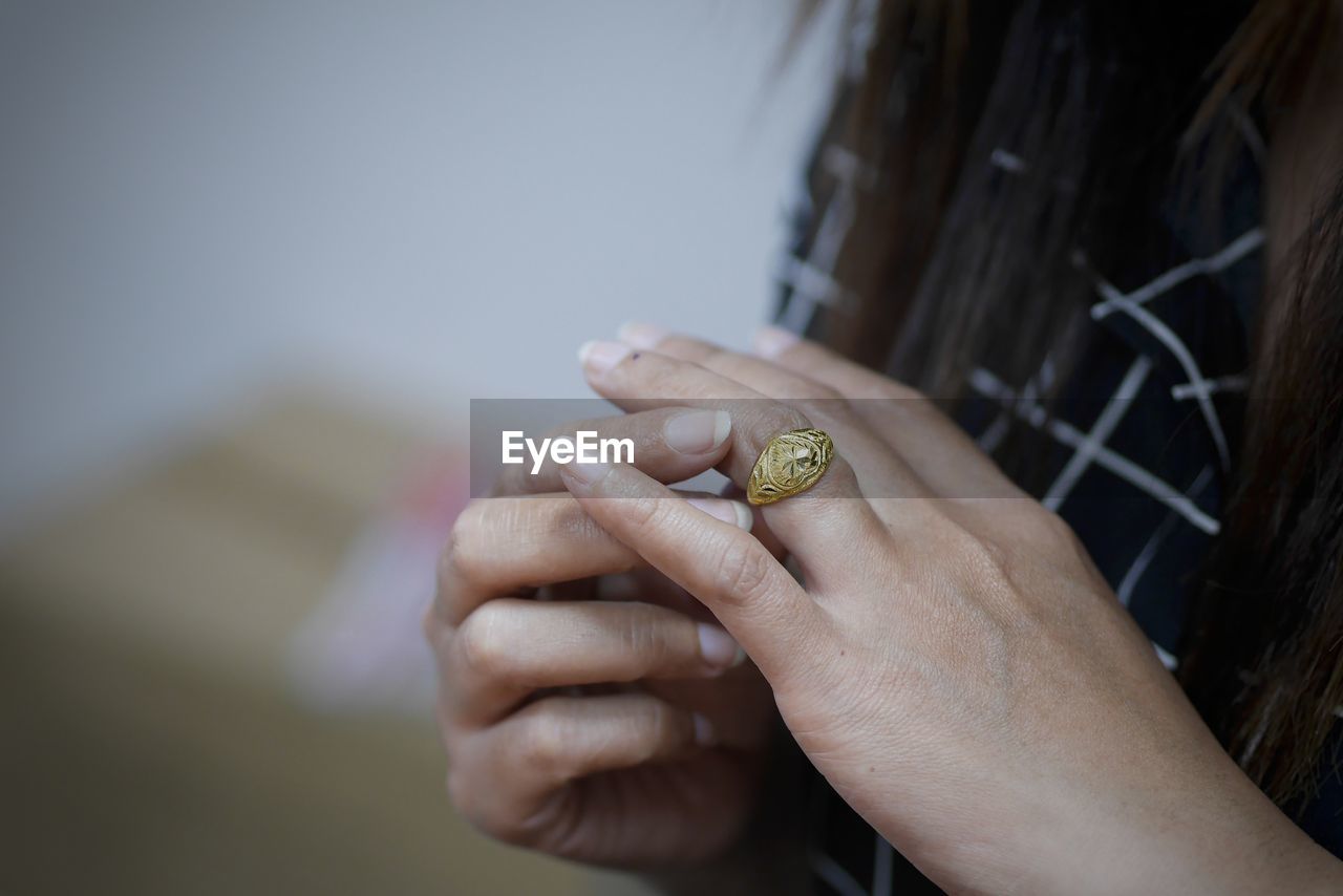 Midsection of woman wearing gold finger ring at home