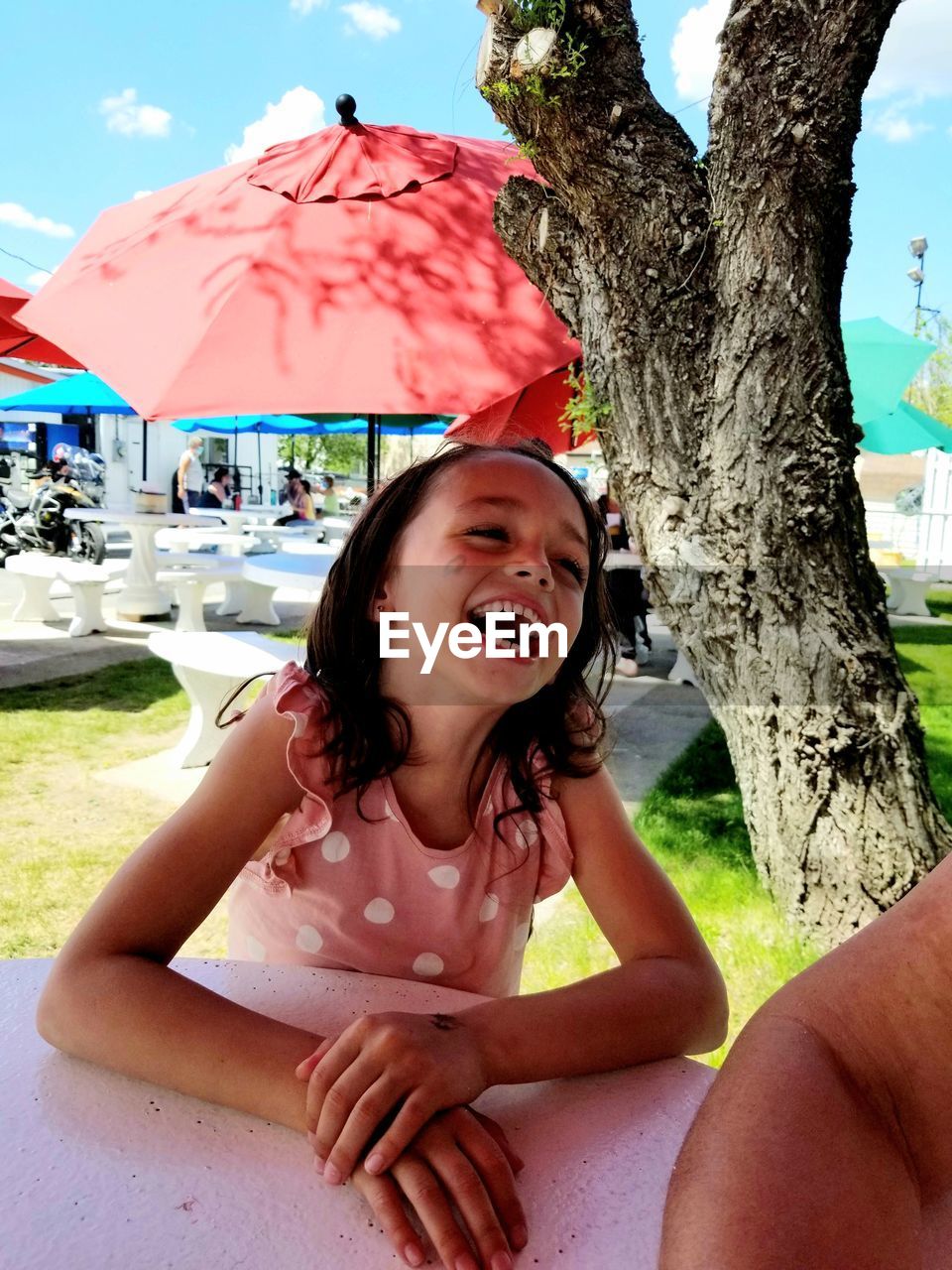 one person, women, happiness, smiling, emotion, leisure activity, nature, sitting, adult, tree, summer, plant, day, portrait, enjoyment, fun, cheerful, umbrella, relaxation, lifestyles, young adult, laughing, female, mouth open, vacation, holiday, outdoors, sunlight, carefree, fashion accessory, trip, sky, person, child, front view, three quarter length, clothing, positive emotion, tree trunk, childhood, looking at camera, land, casual clothing, spring, trunk, hairstyle, human mouth, teeth, eyes closed