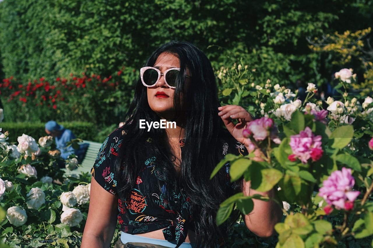 Young woman wearing sunglasses while standing amidst flowers at park