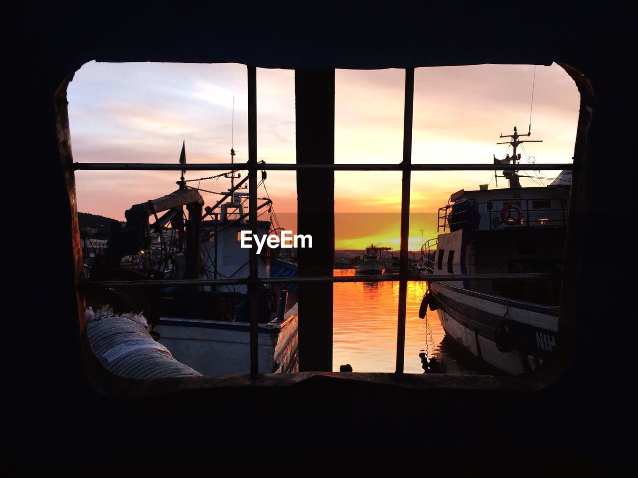 Boats at harbor seen through window during sunset