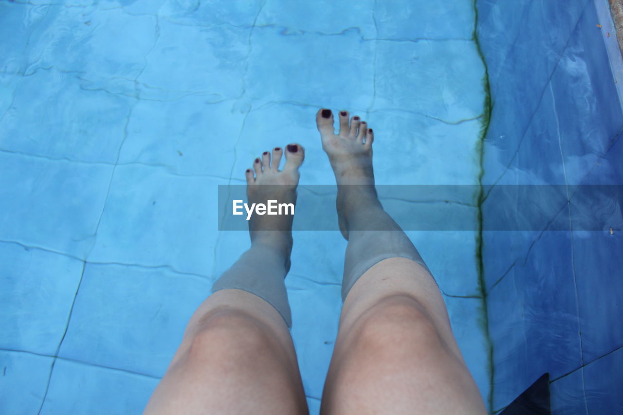 LOW SECTION OF WOMAN LEGS AGAINST BLUE SWIMMING POOL
