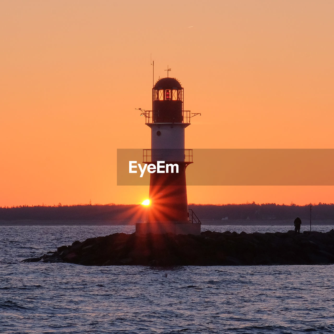 Lighthouse by sea against clear sky during sunset