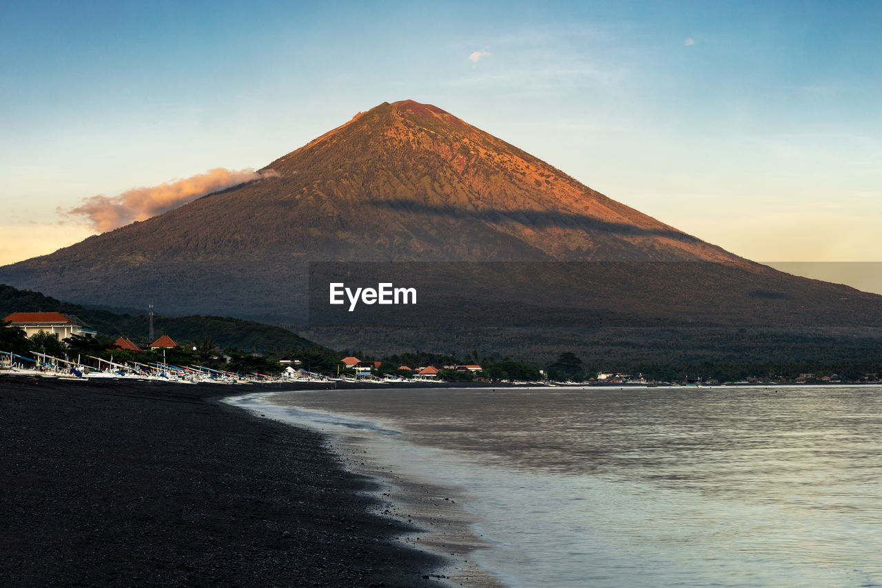 Sunrise at the black sand beach coast of amed, bali and mount agung volcano in the background