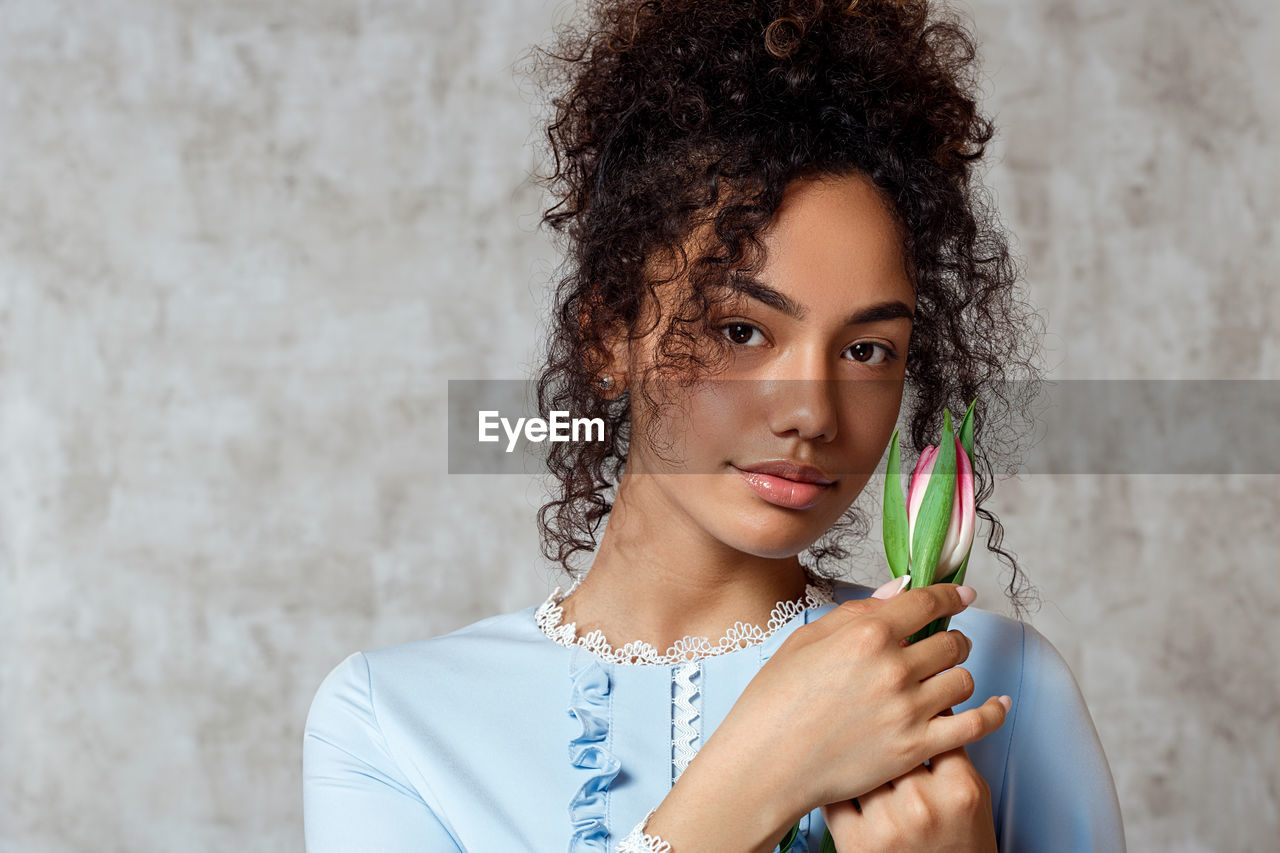 Portrait of smiling young woman holding tulip while standing against wall