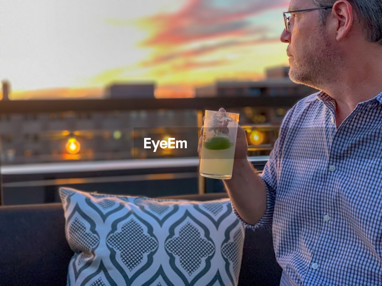 Mature man having drink against sky during sunset