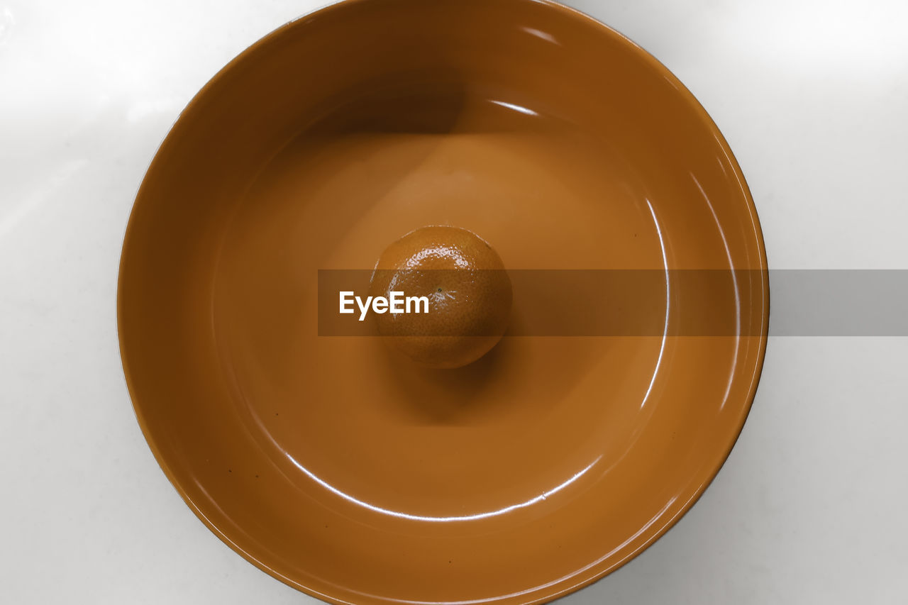 Mandarin in orange colored circular bowl, minimal still life