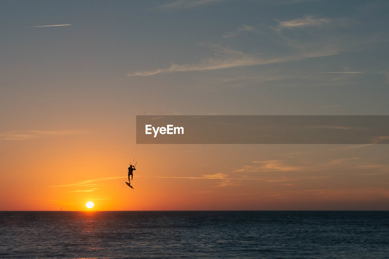 Scenic view of sea against sky during sunset with kitesurfer silohuette