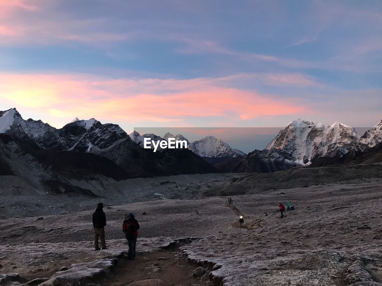 People walking on land against sky during sunset