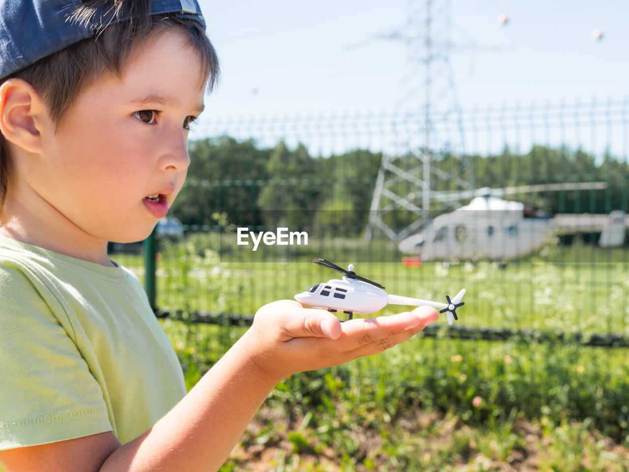 Little boy holds toy helicopter in front of real one on helipad. kid dreams of becoming a pilot. 