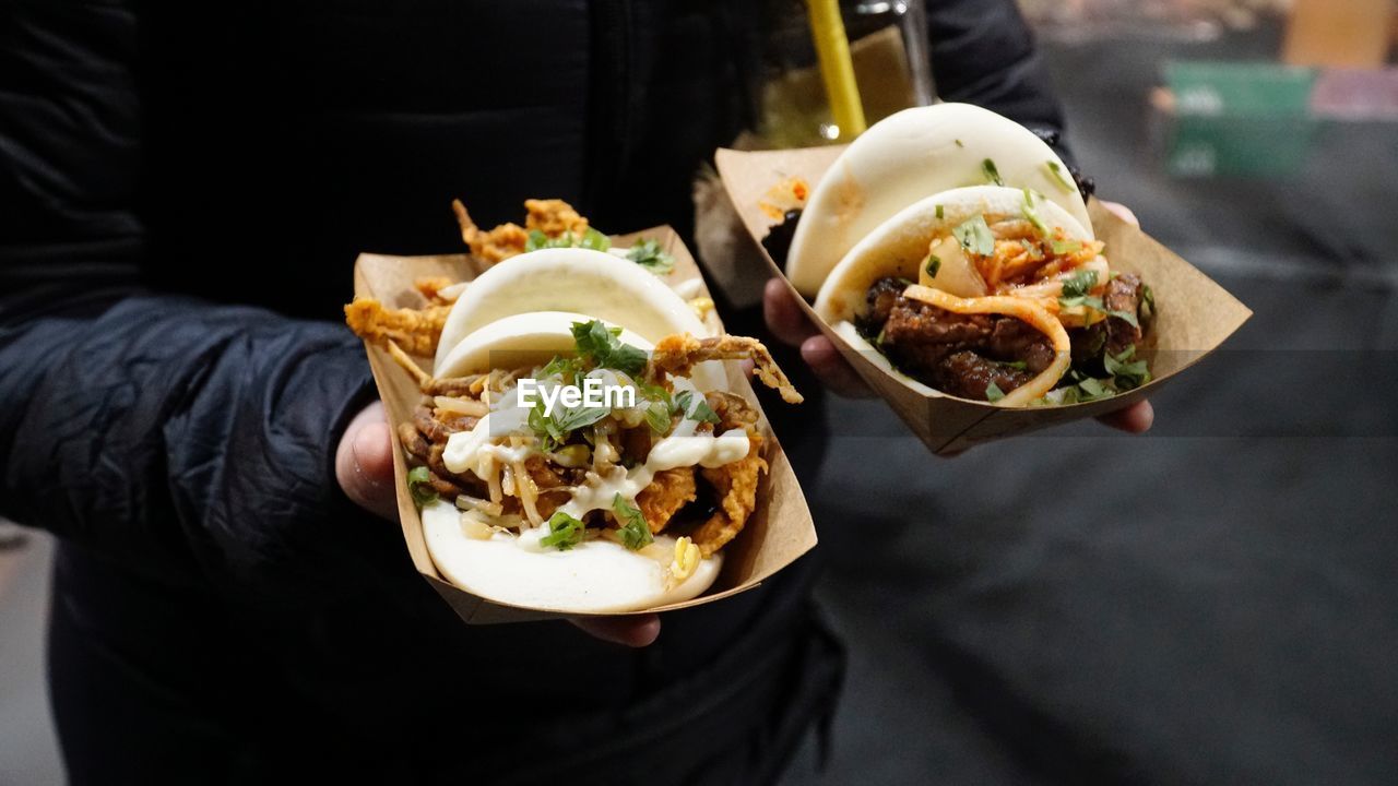 Midsection of person holding burgers in containers