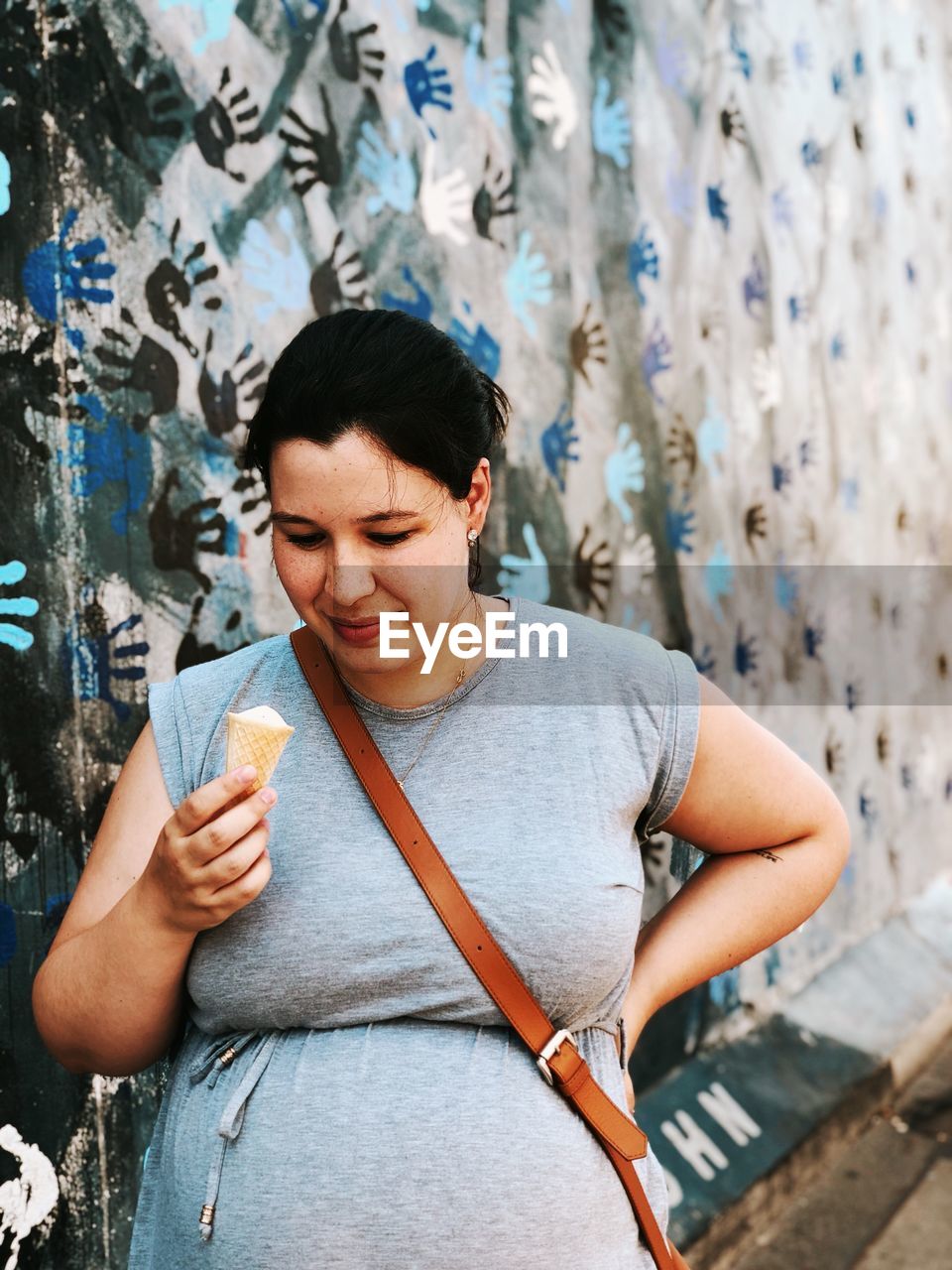 Pregnant woman having ice cream cone against wall