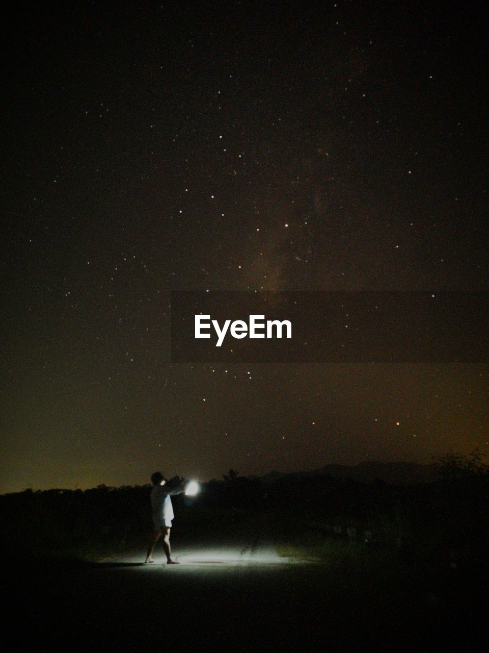 Silhouette man with flashlight standing on field against star field at night
