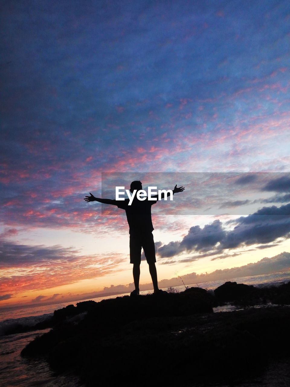 REAR VIEW OF SILHOUETTE MAN STANDING ON SHORE AGAINST SKY DURING SUNSET