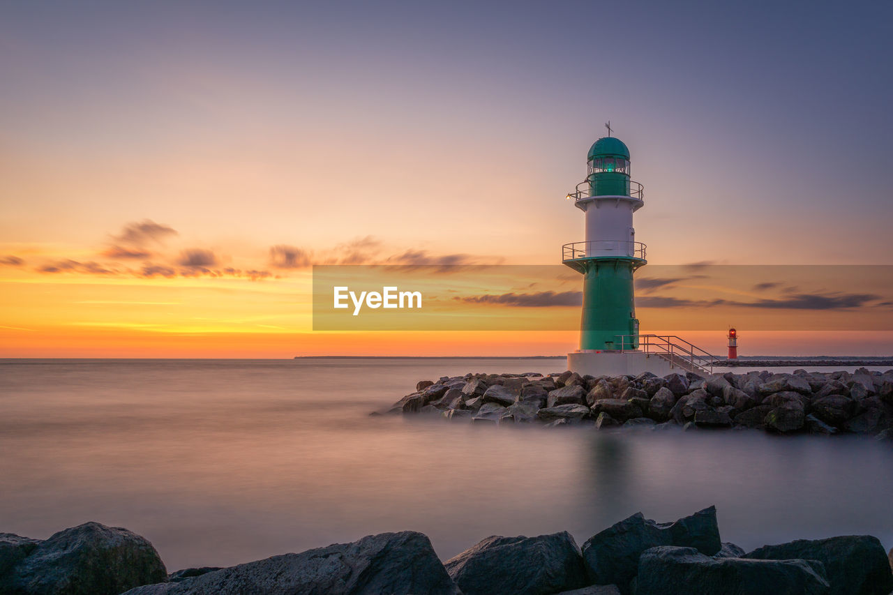 Lighthouse by sea against sky during sunset