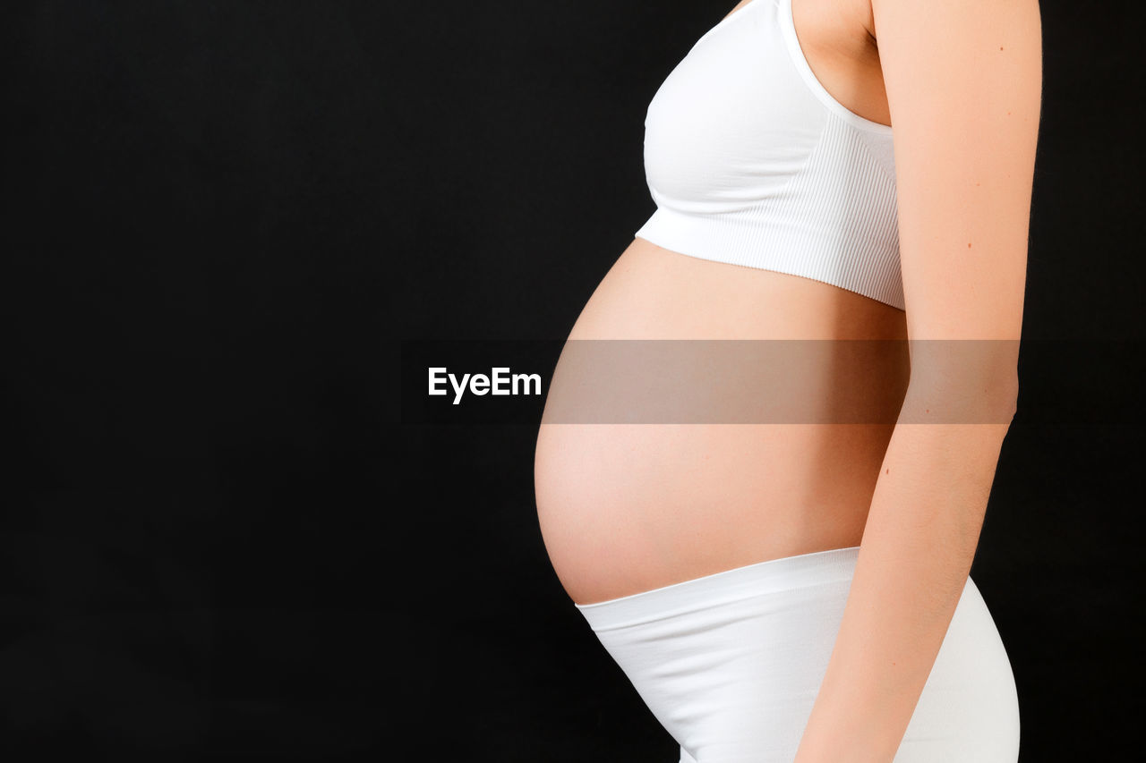 MIDSECTION OF A WOMAN AGAINST BLACK BACKGROUND