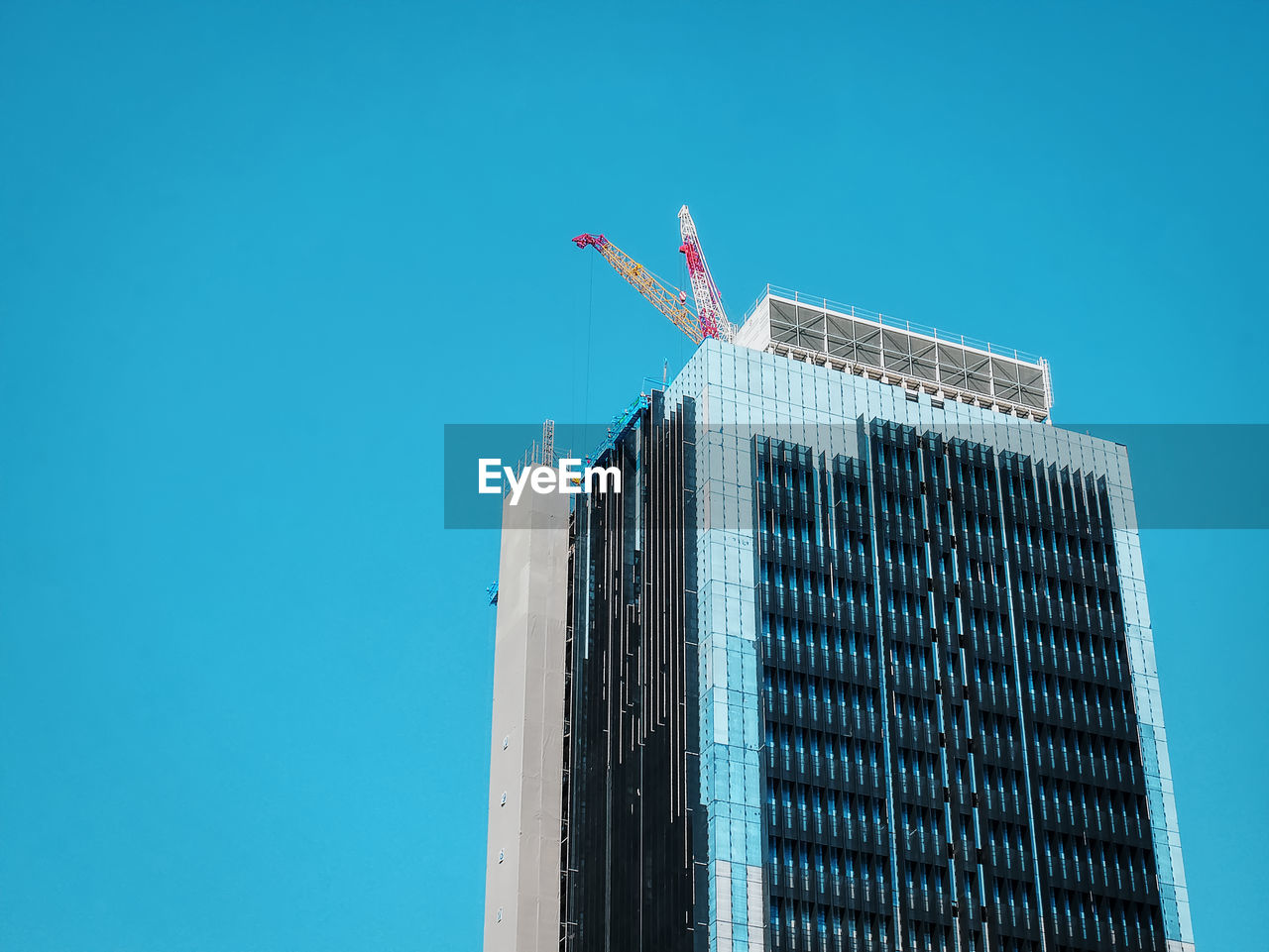 Low angle view of under construction building with cranes on the roof floor