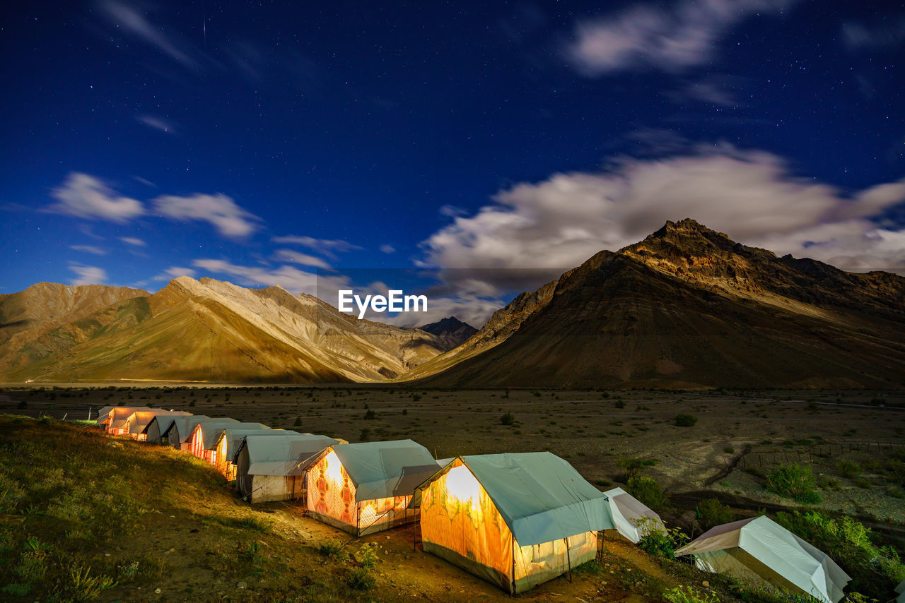 Illuminated tents by mountains against sky at dusk