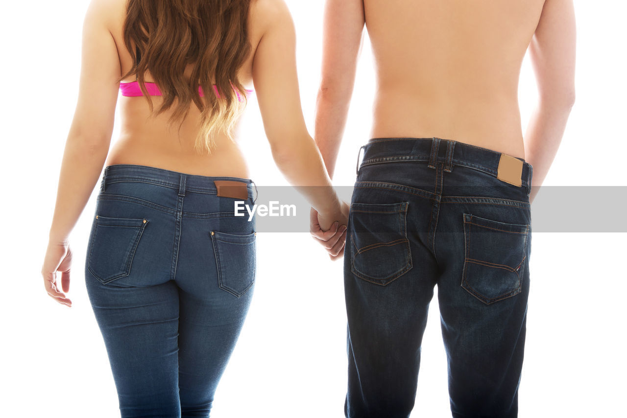 Rear view of shirtless man and woman holding hands while standing against white background