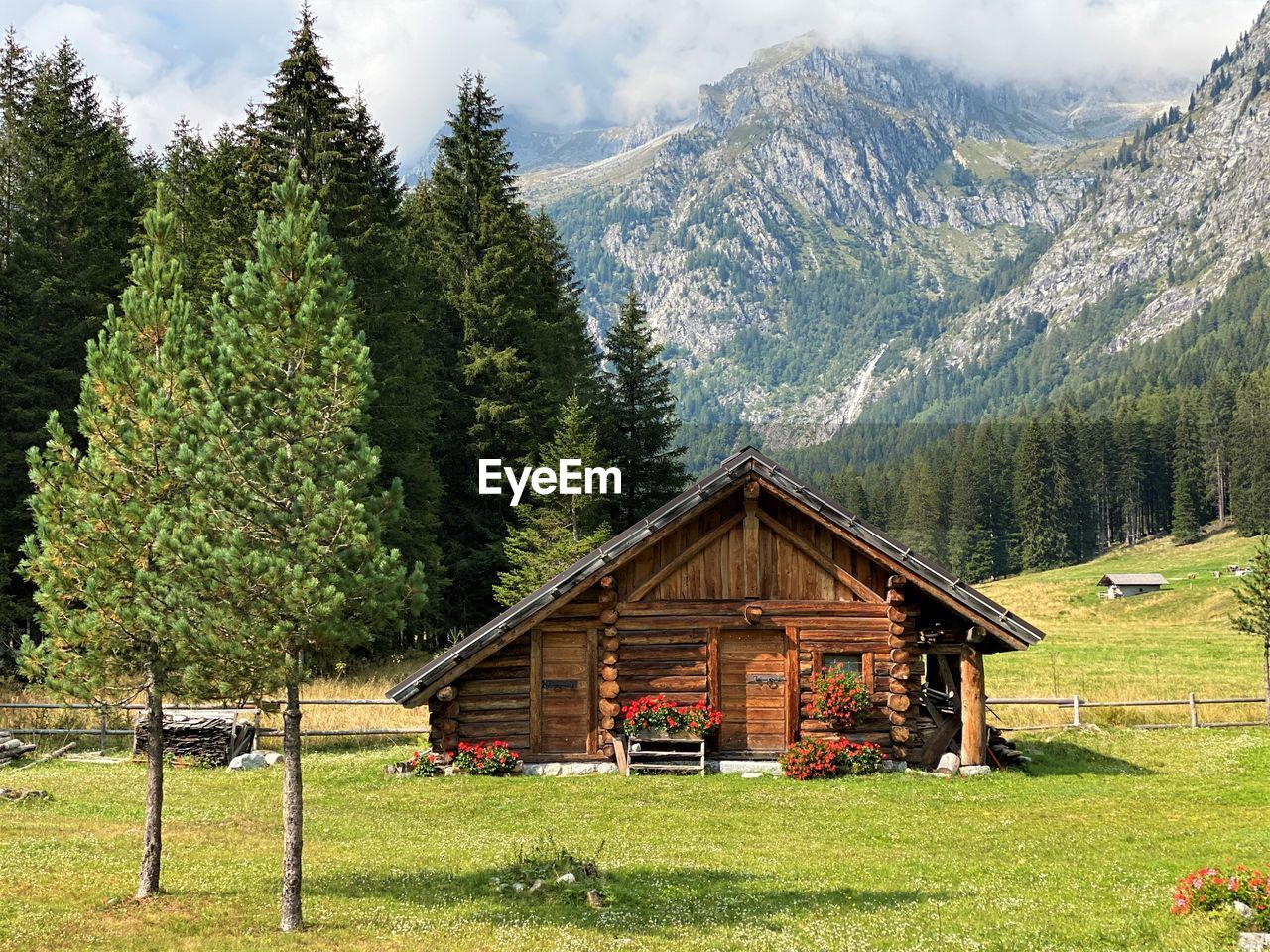 HOUSE ON FIELD BY TREES AND MOUNTAINS AGAINST SKY