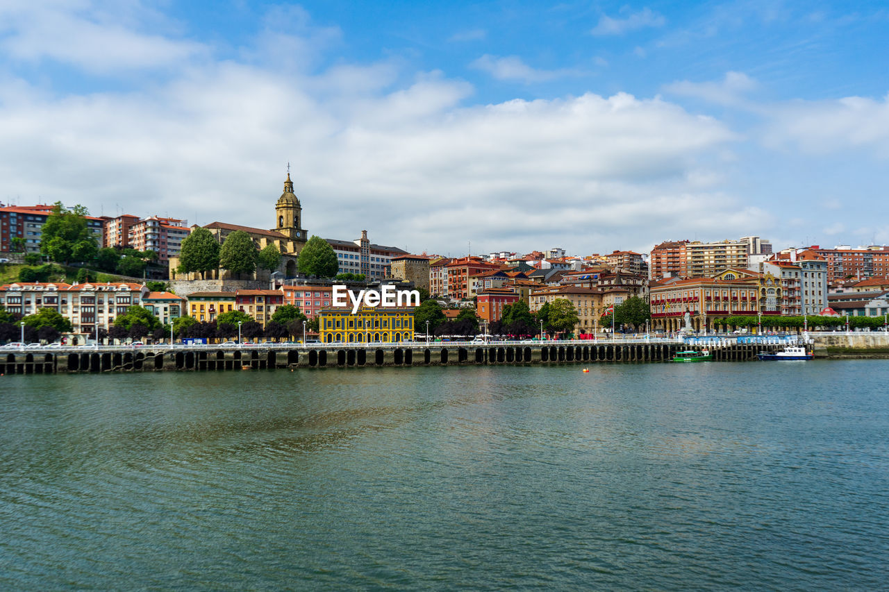 buildings by river against sky in background