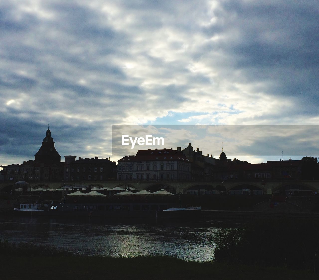 CITY AT WATERFRONT AGAINST CLOUDY SKY