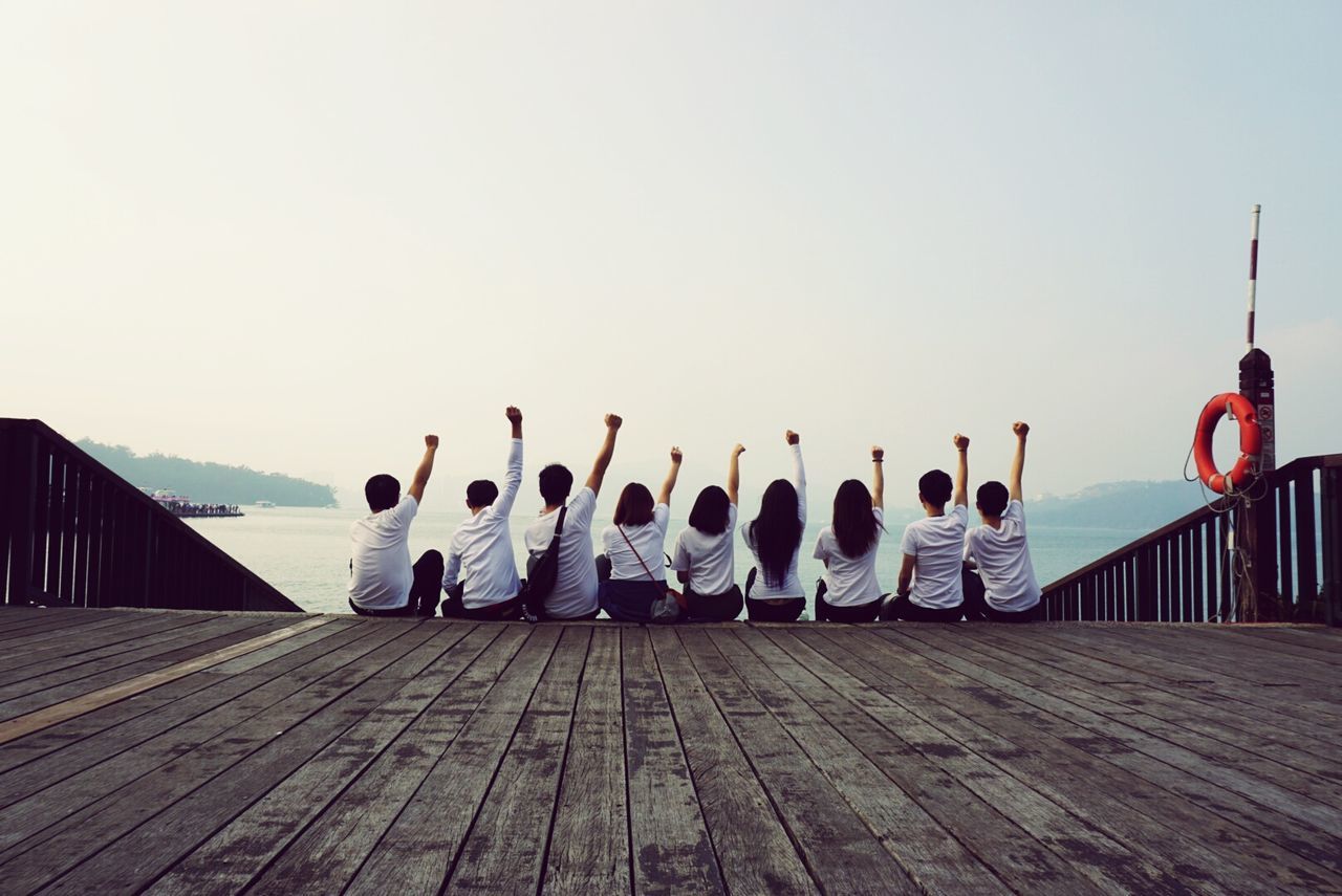 Rear view of friends with arms raised on boardwalk against sky