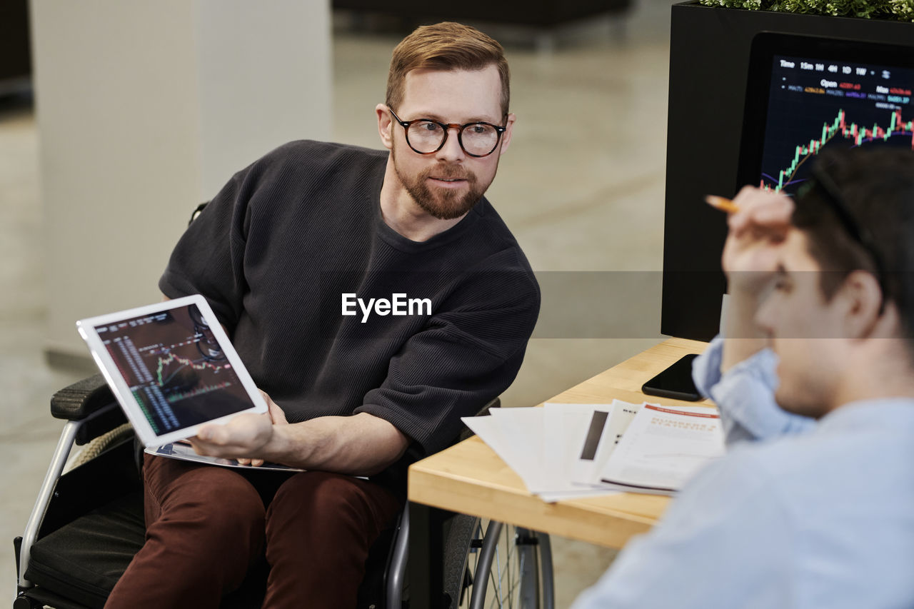 Disabled businessman showing cryptocurrency graph on tablet pc to colleague in office