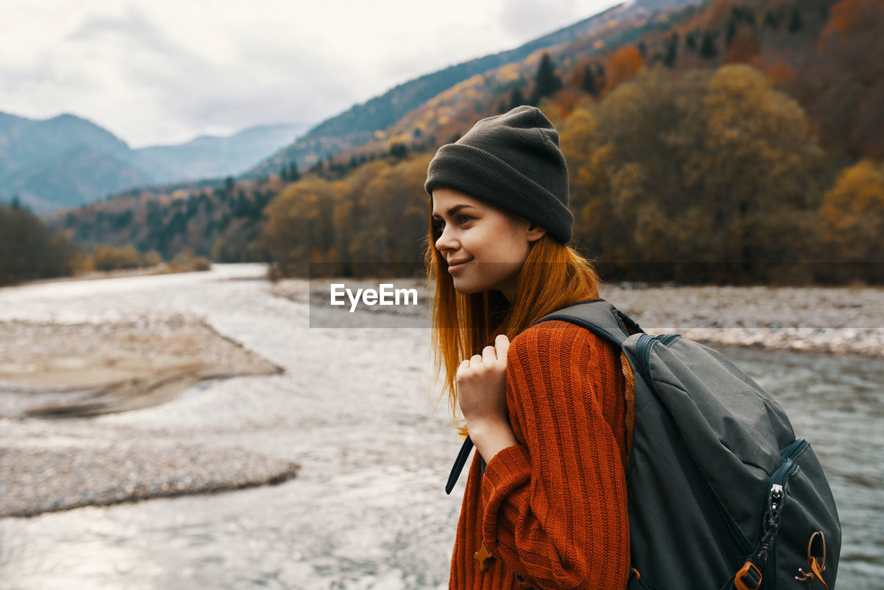 YOUNG WOMAN STANDING AGAINST MOUNTAINS