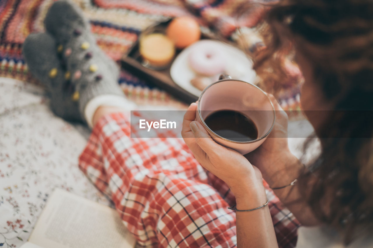 High angle view of woman holding coffee cup on bed