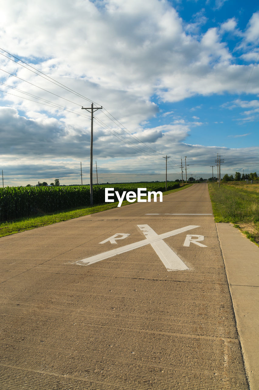 High angle view of railroad crossing sign on road against cloudy sky during sunny day