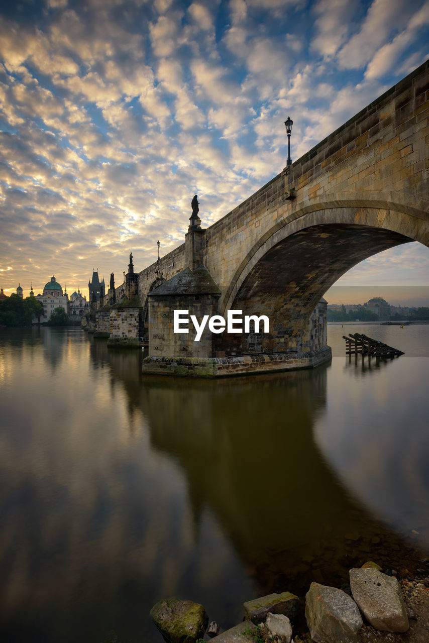 Arch bridge over river by buildings against sky