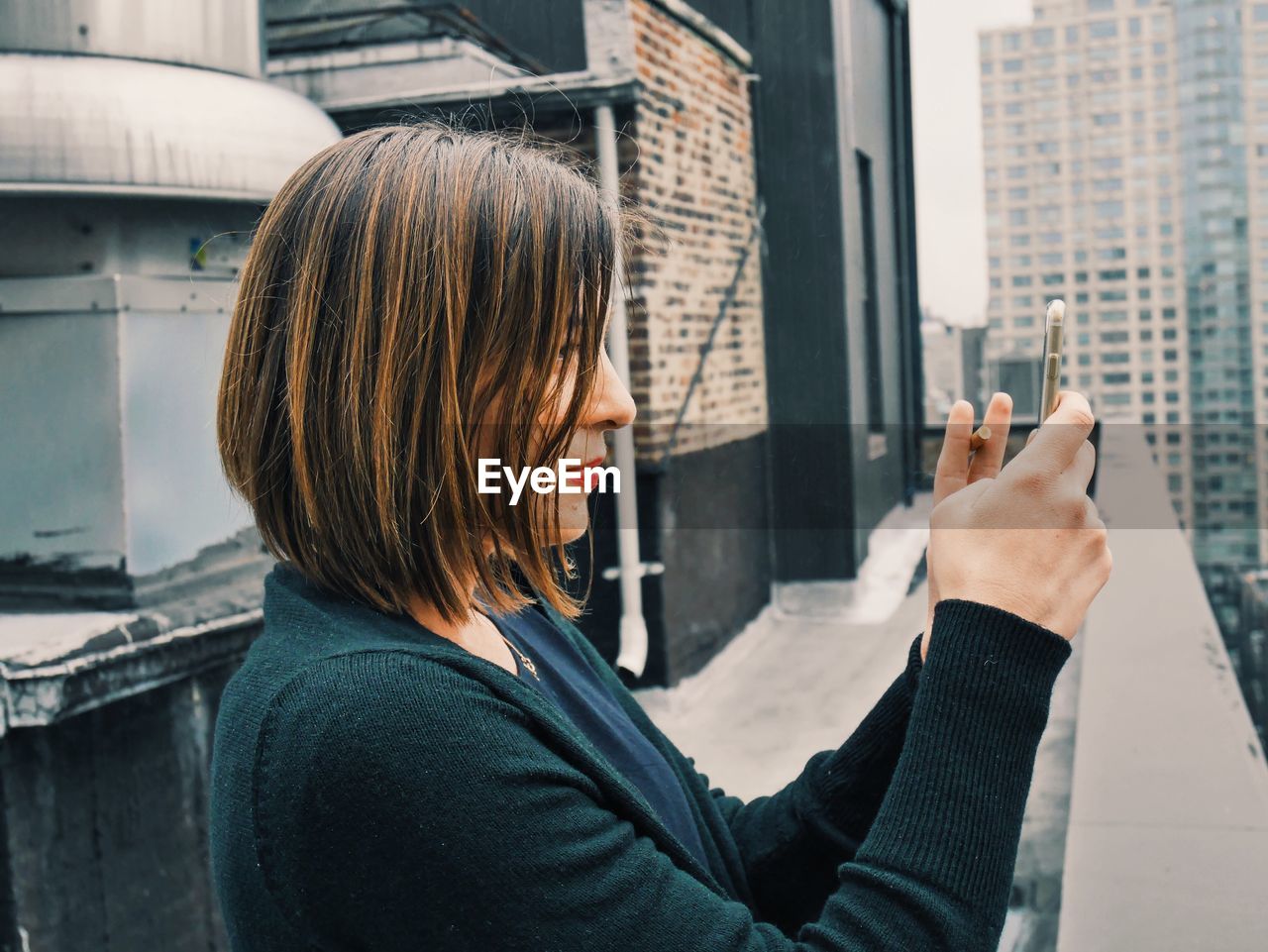 Woman taking photo with smart phone from rooftop balcony