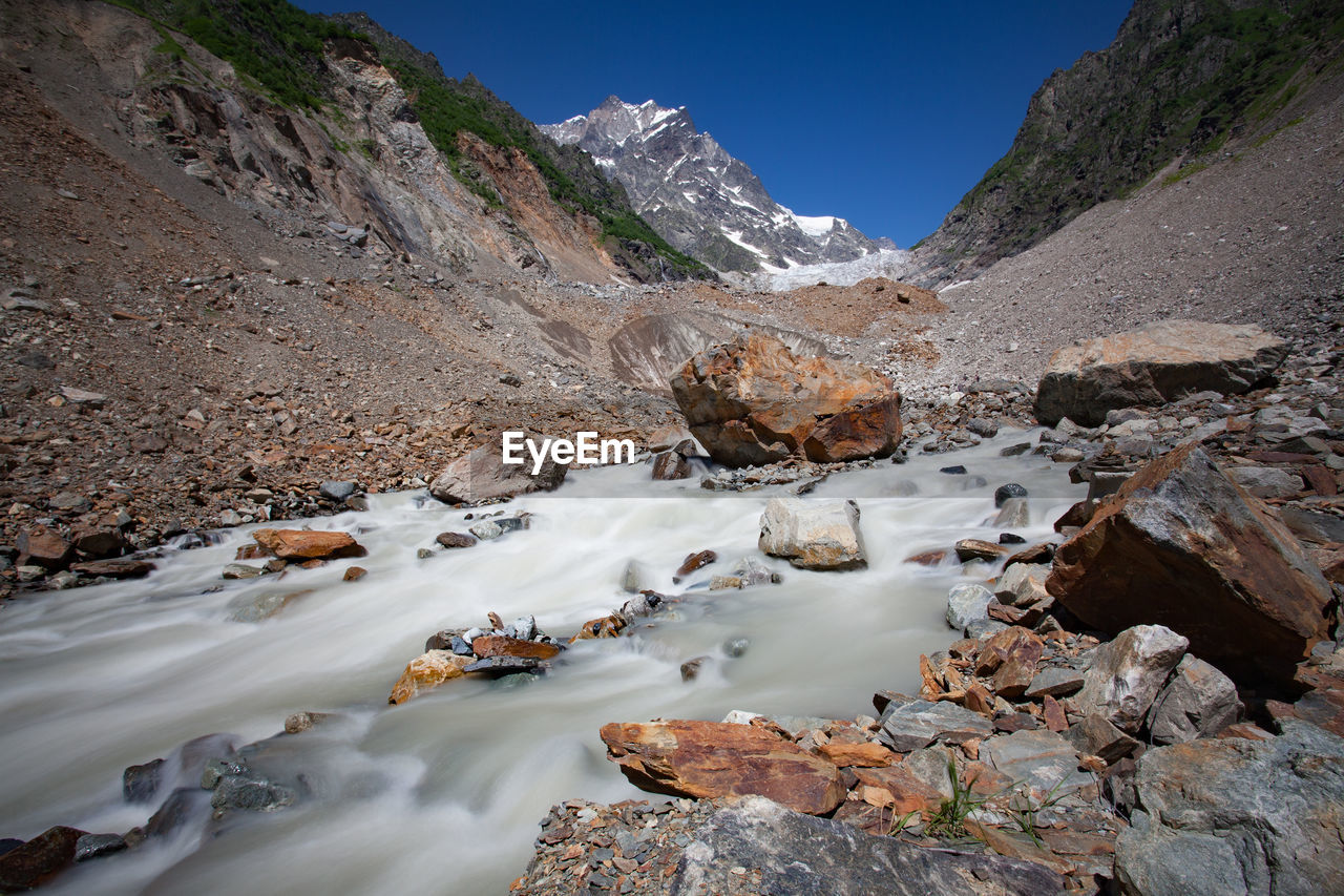 Scenic view of stream flowing through rocks against sky