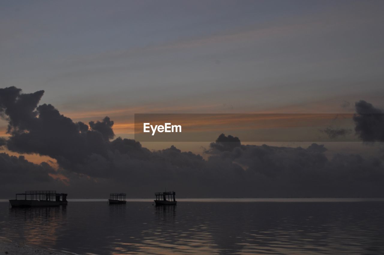 Silhouette boats in sea against sky during sunset