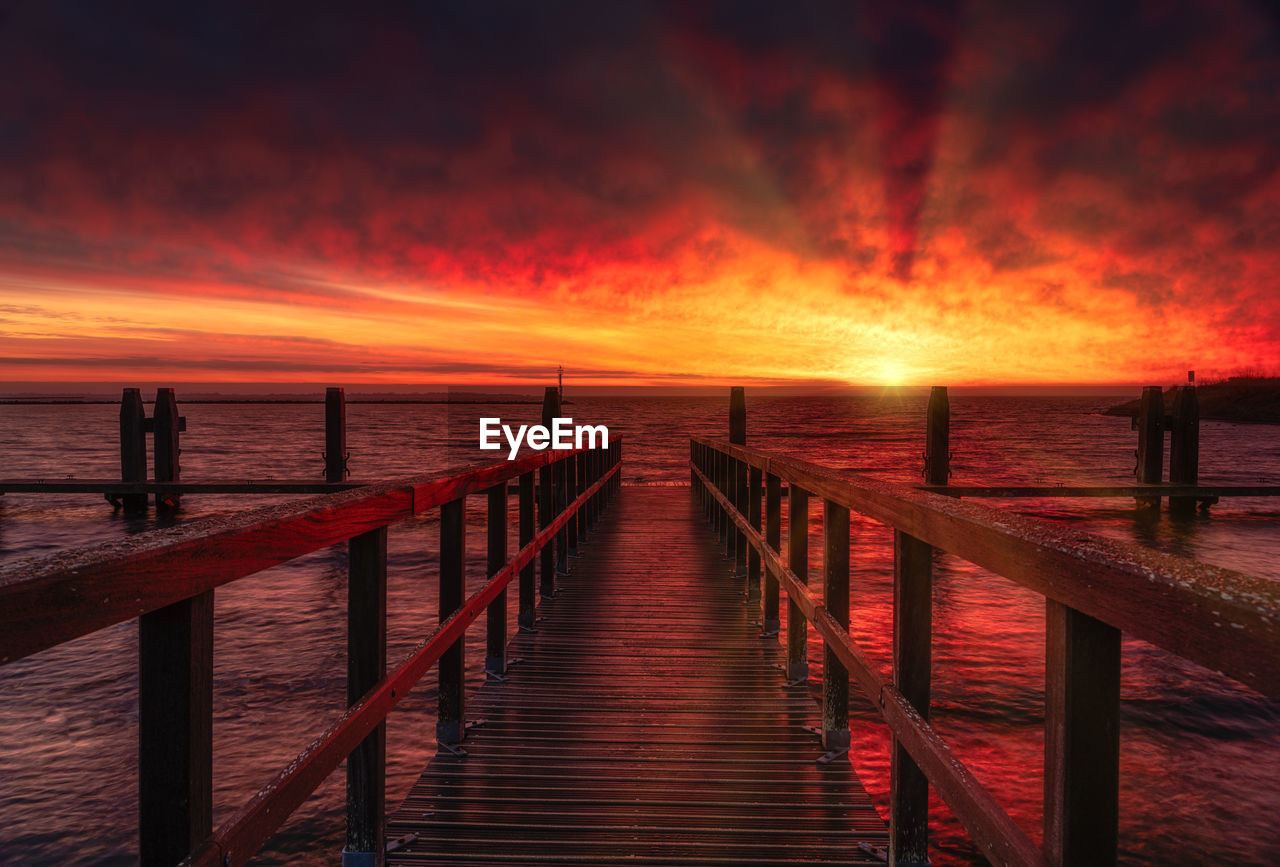 Pier over sea against orange sky