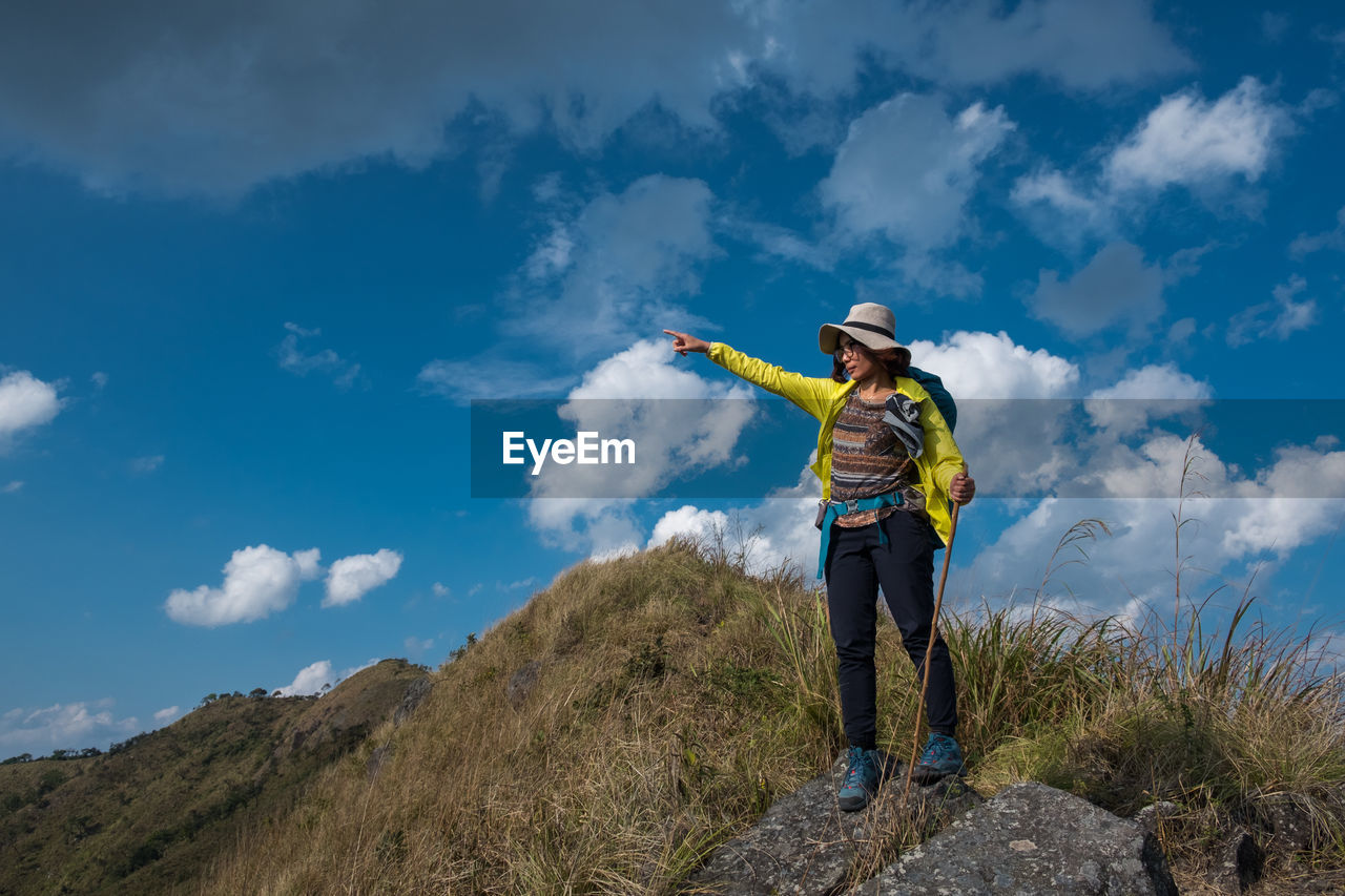 Mid adult woman gesturing on mountain against cloudy sky