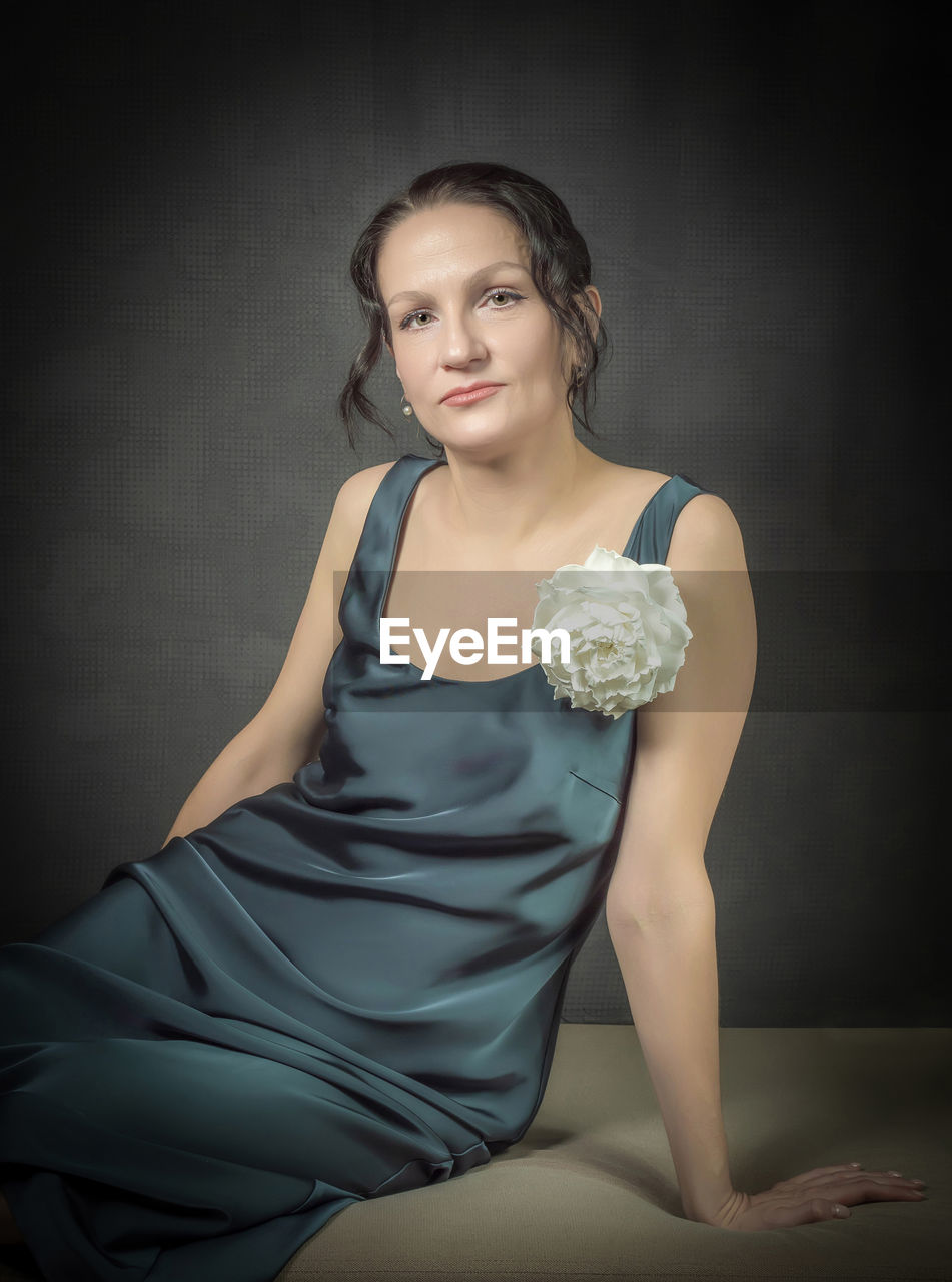 A beautiful girl in an evening gown is sitting against a gray wall