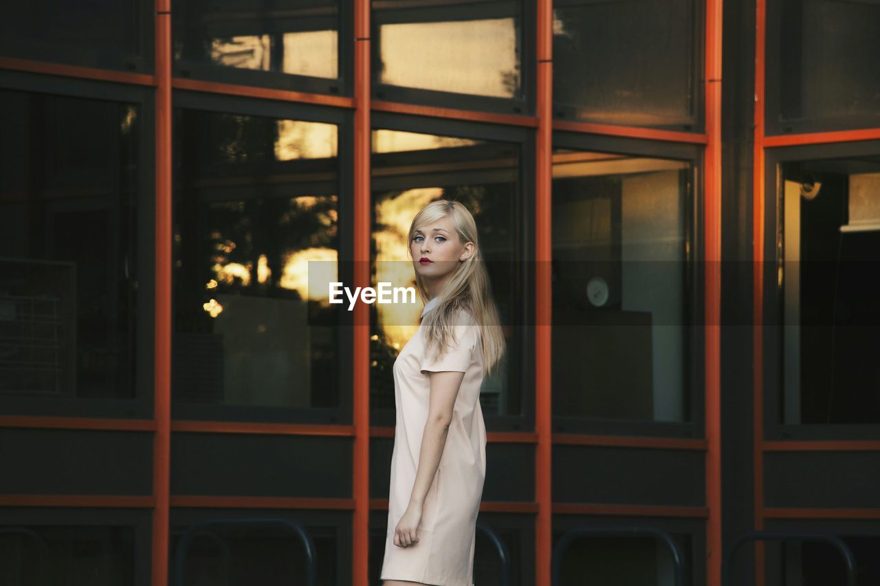 Portrait of young woman standing by glass building