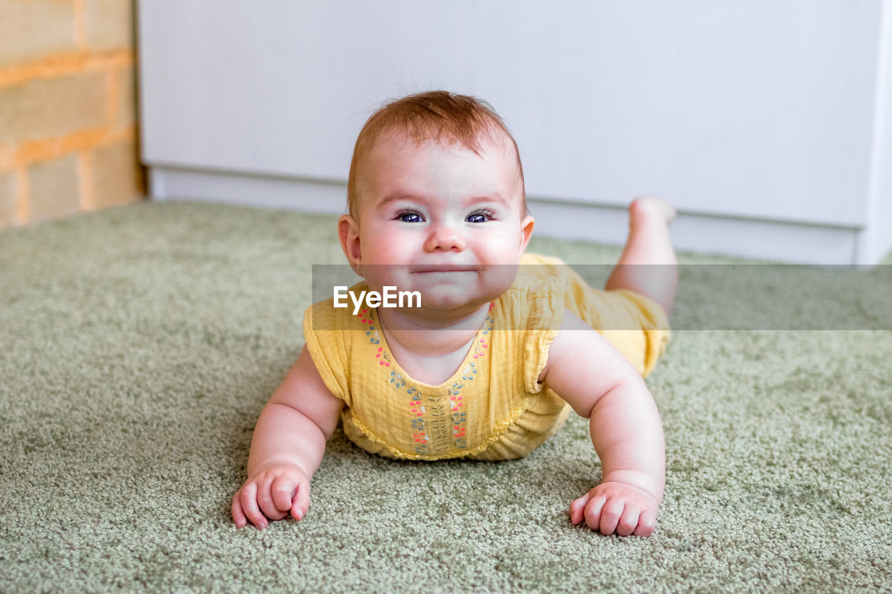 Portrait of smiling little caucasian baby girl in yellow dress. child trying to crawl on a floor.