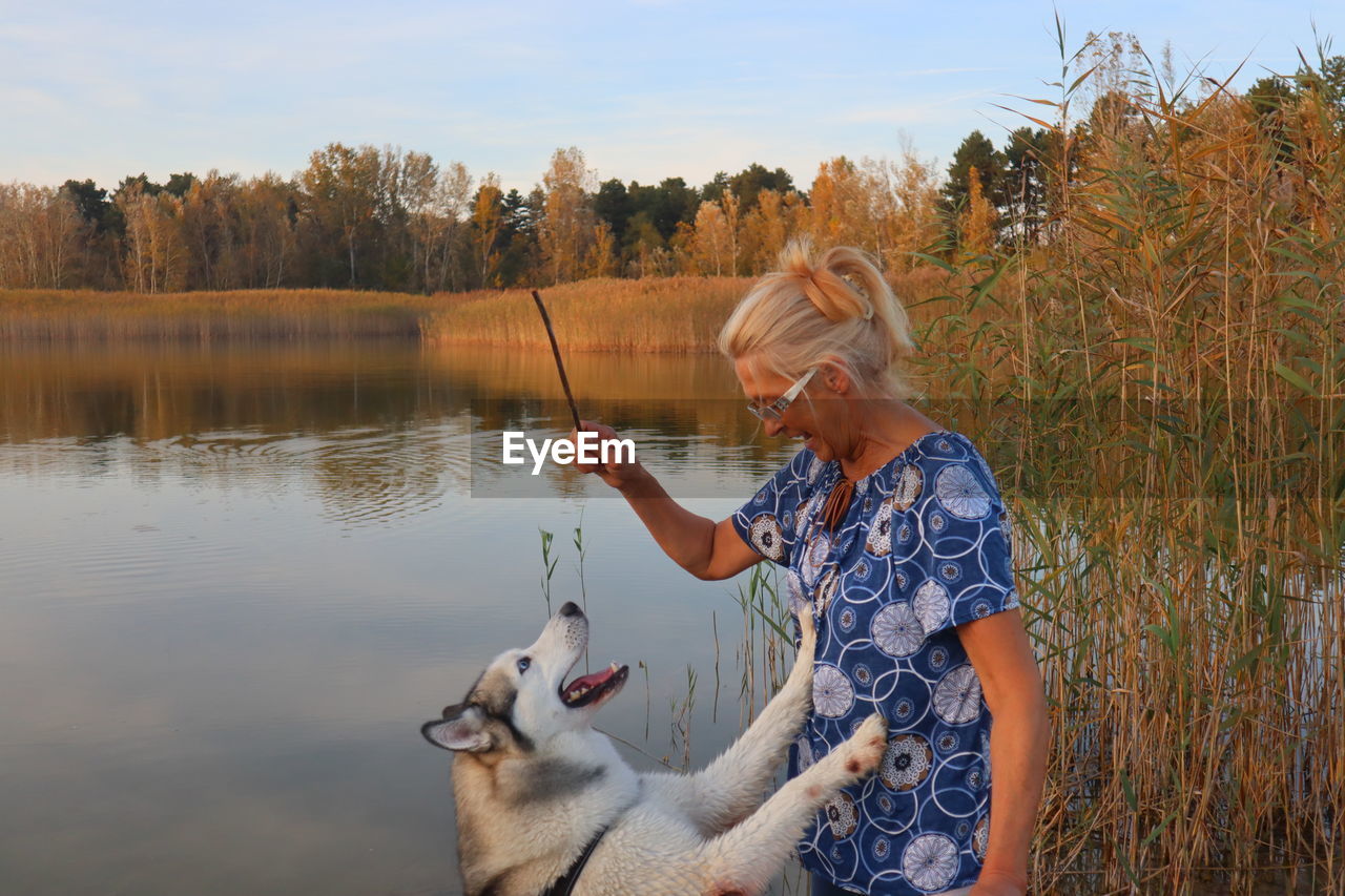 Senior woman playing with dog against lake