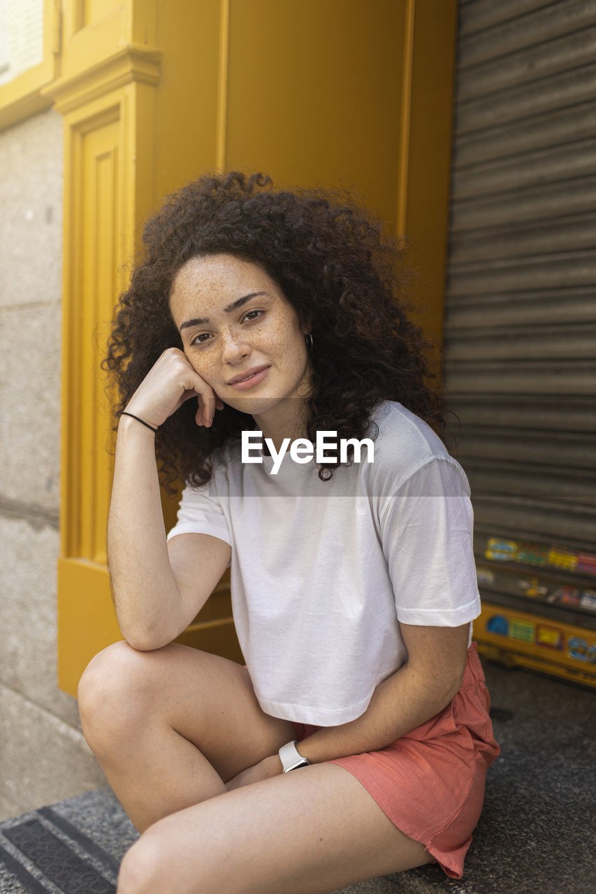 Young woman with curly hair sitting in front of shutter