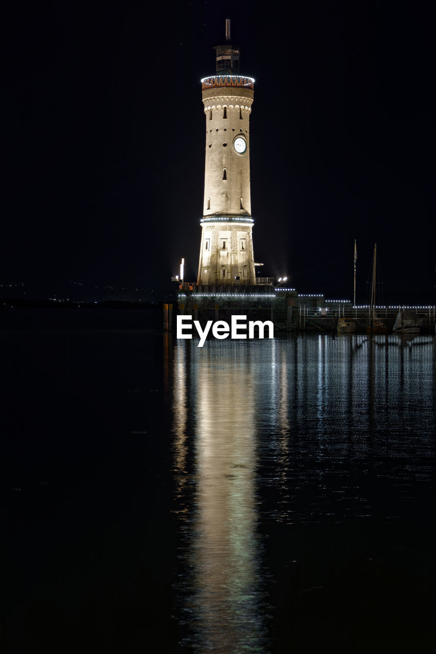 ILLUMINATED LIGHTHOUSE BY BUILDING AT NIGHT