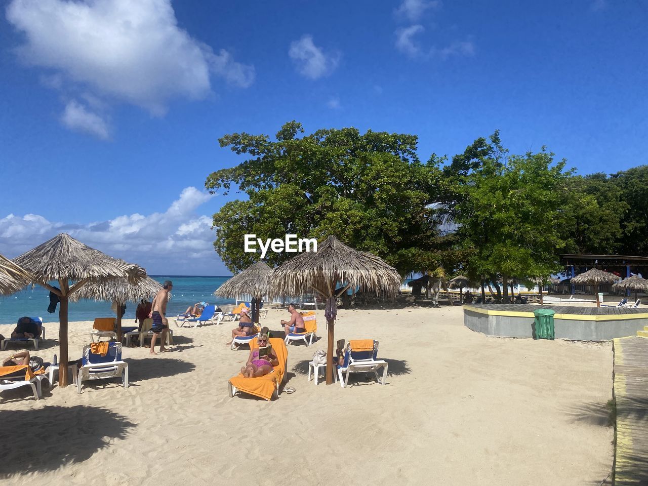 sky, beach, land, nature, tree, sand, water, vacation, chair, trip, sea, holiday, plant, travel destinations, parasol, cloud, summer, sunshade, sunlight, lounge chair, relaxation, body of water, day, travel, beauty in nature, resort, umbrella, beach umbrella, thatched roof, seat, tropical climate, scenics - nature, blue, outdoors, shade, tourism, group of people, architecture, sunny, leisure activity, hut, coast, tranquility, shore, tourist resort, shadow, ocean, tourist