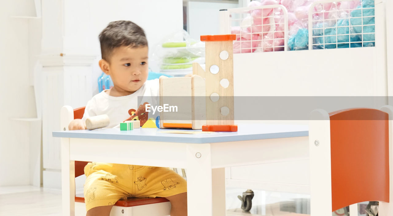 Cute boy playing with toys while sitting on table at home