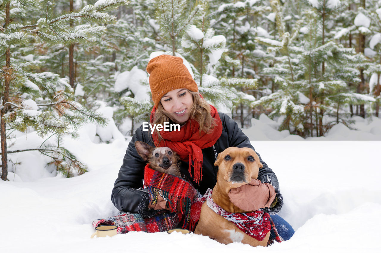 Woman with dogs on snow field against trees during winter