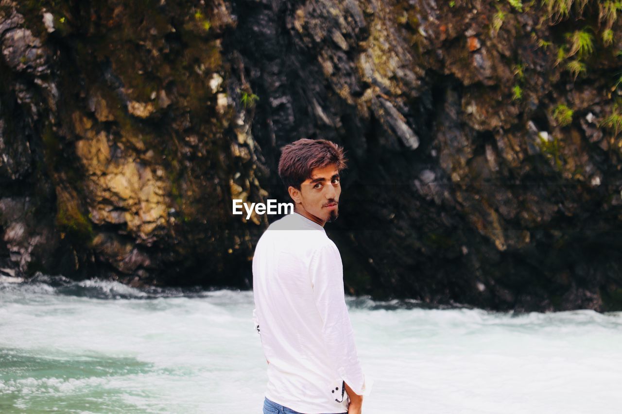 Portrait of young man standing against riverbank