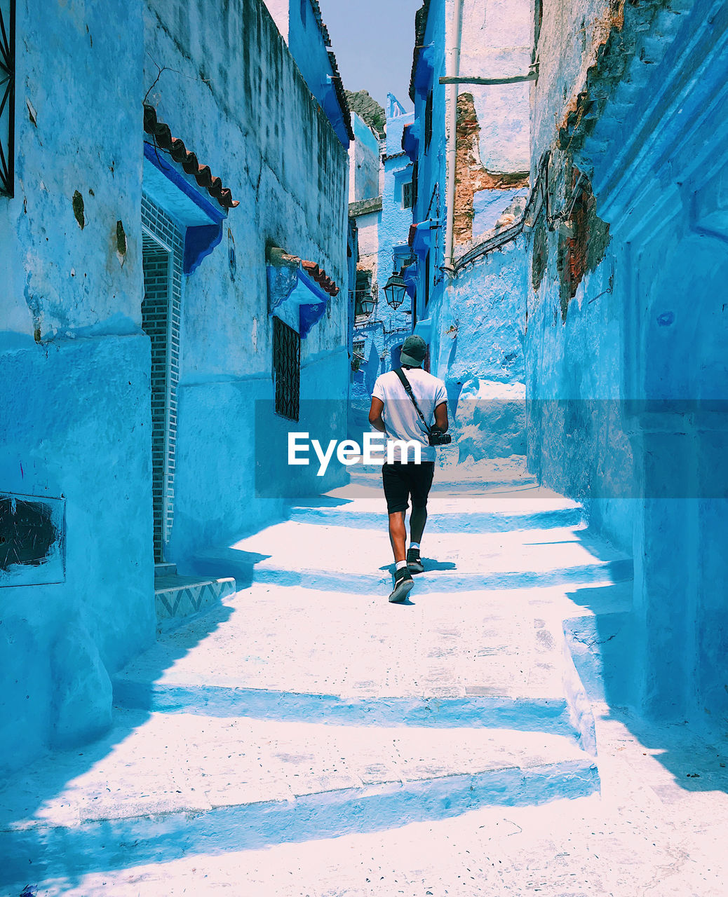 Rear view of man walking on alley amidst buildings in city