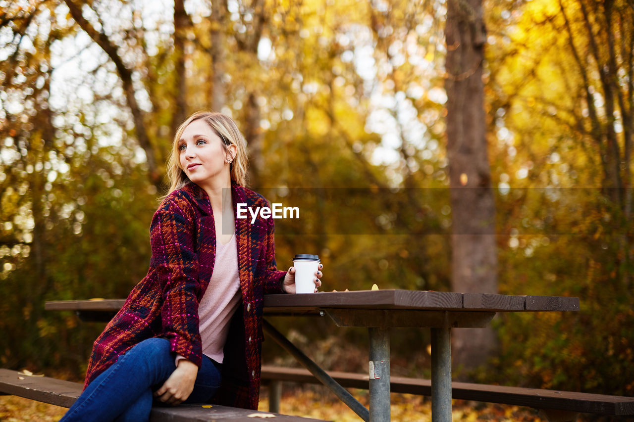 Young woman sitting on picnic table in park during autumn